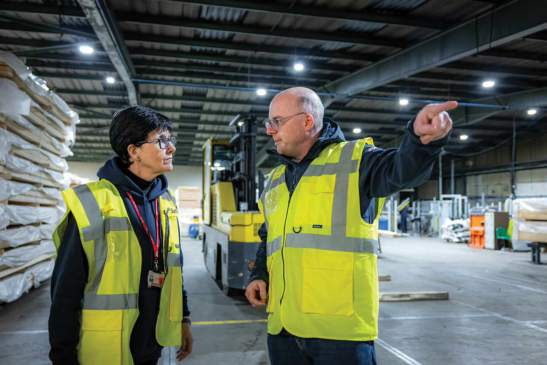 A man and woman in a warehouse in hi-vis jackets